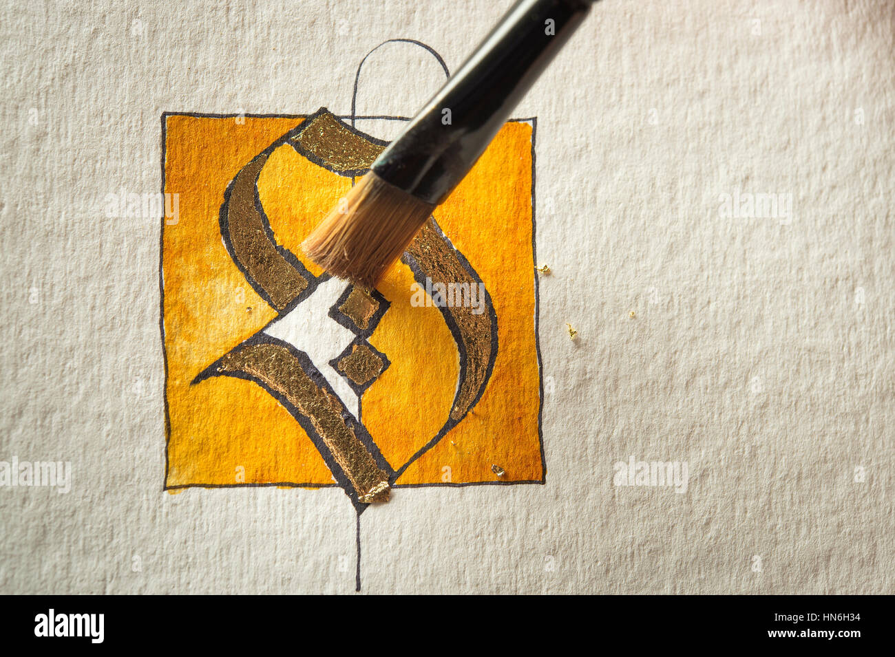 Calligraphy studio, paintbrush removing residual transfer gold, letters S coated with gold on