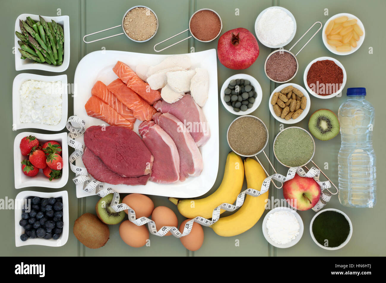 Body building healthy food collection of meat, fish, supplement powders,vitamin pills,fruit, dairy, bottled water and tape measure over slate backgrou Stock Photo