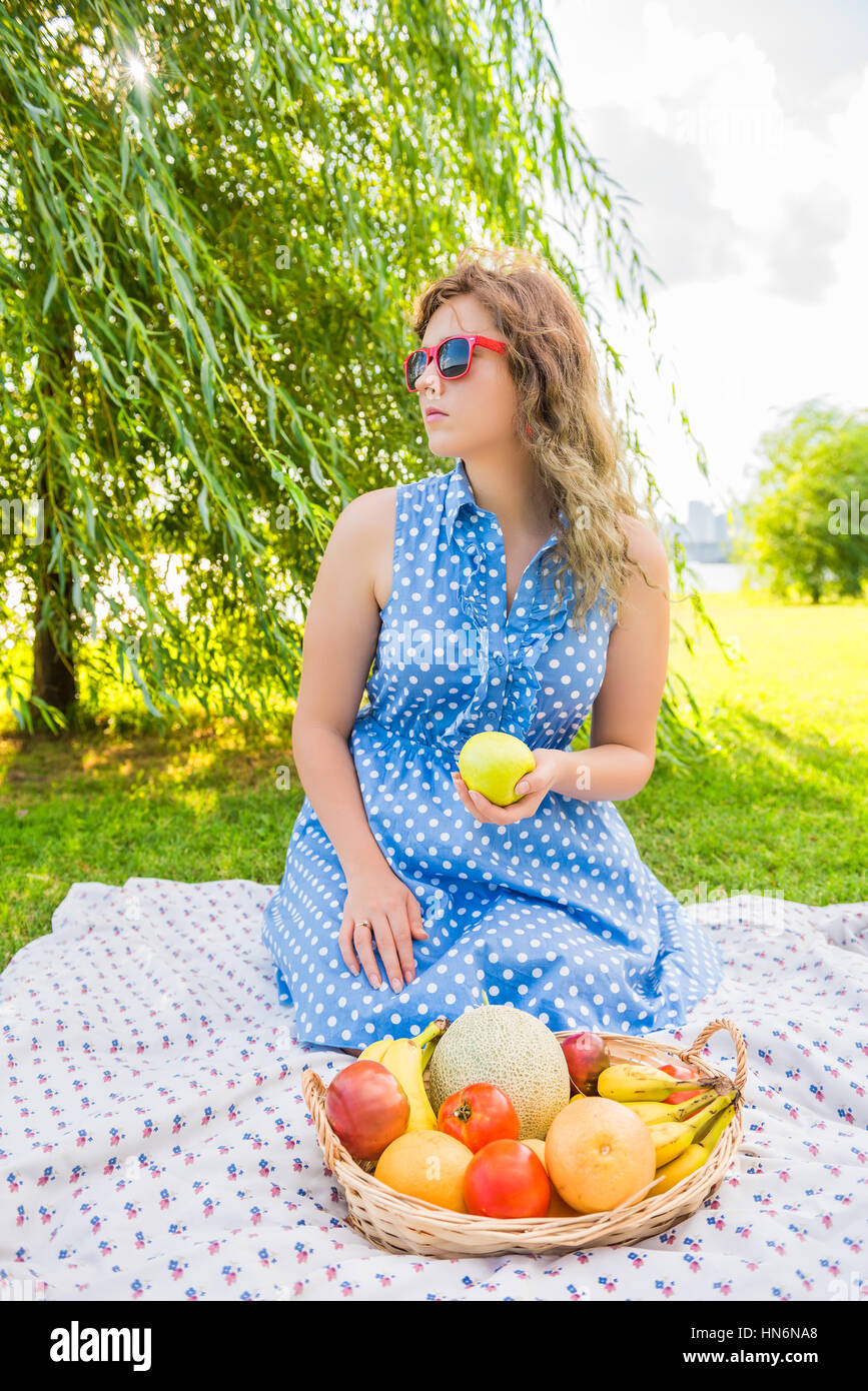 Young girl in dress and red sunglasses sitting on picnic blanket