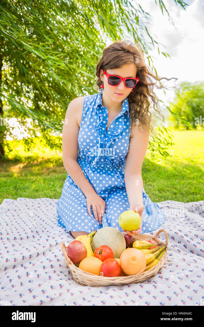 Young girl in dress and red sunglasses sitting on picnic blanket