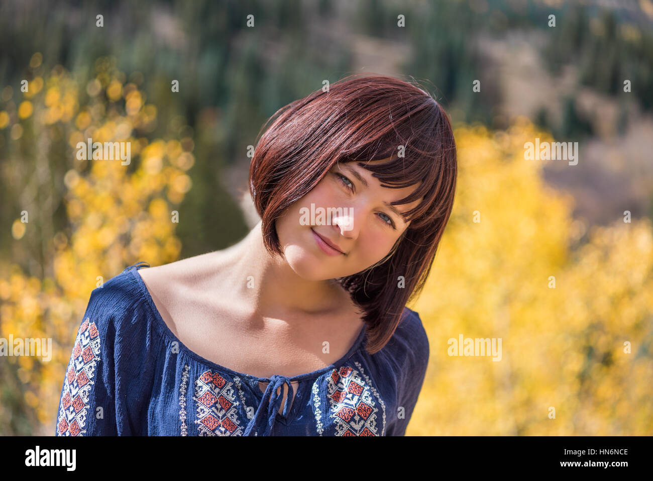 Portrait of young happy smiling woman with purple plum hair by autumn aspen trees with head tilted Stock Photo