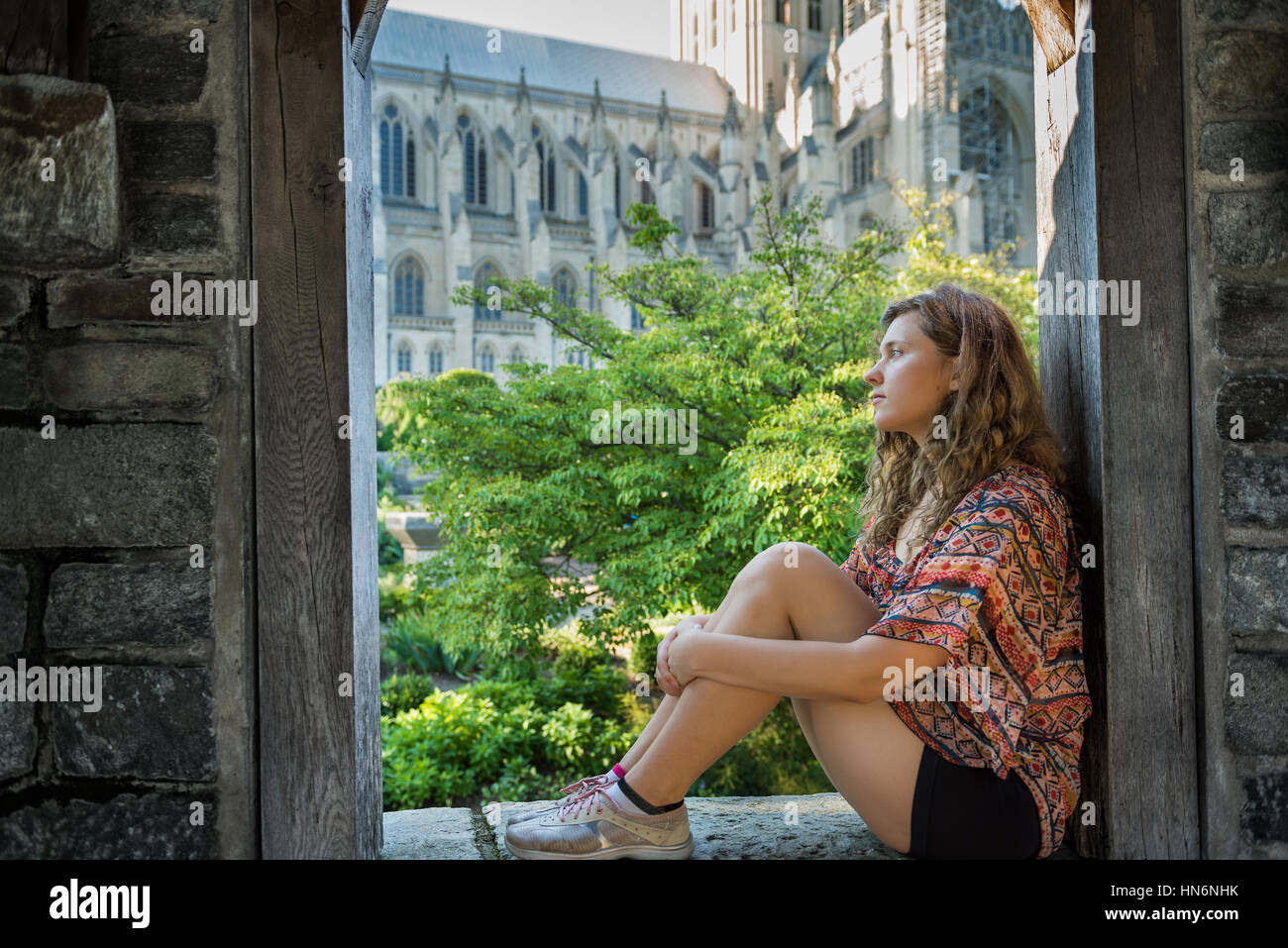 Side profile of young woman sitting on windowsill by church Stock Photo