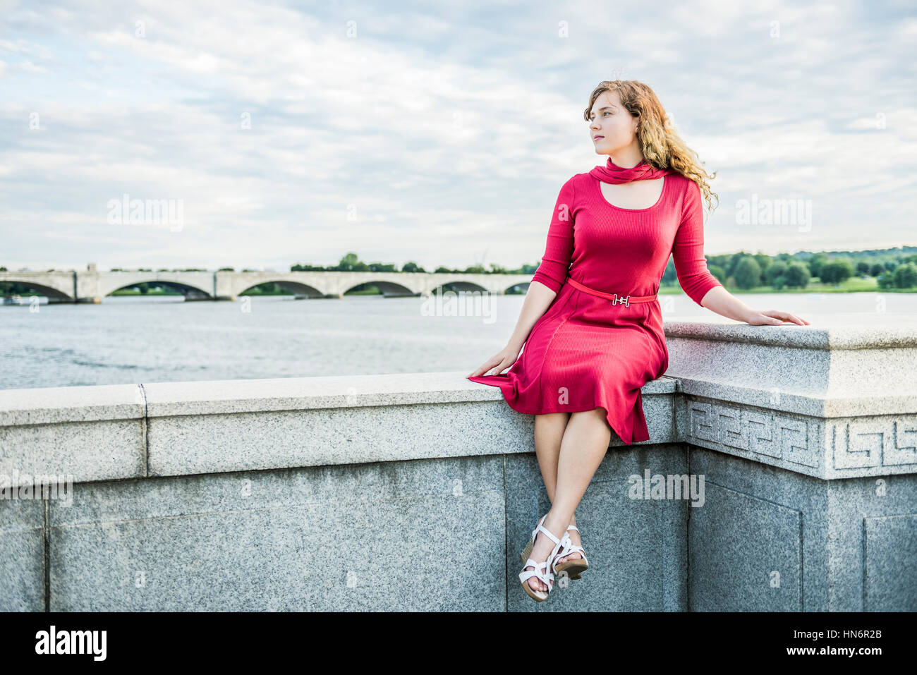 Stone Railing Sitting Young woman in red dress and scarf sitting on stone railing in ...
