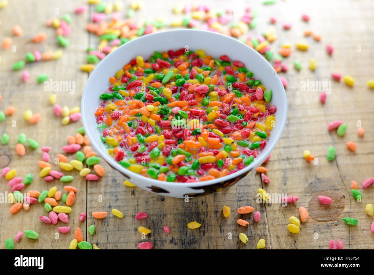 Prepared breakfast with milk and colorful puffed rice in the bowl with spilled rice in the background Stock Photo