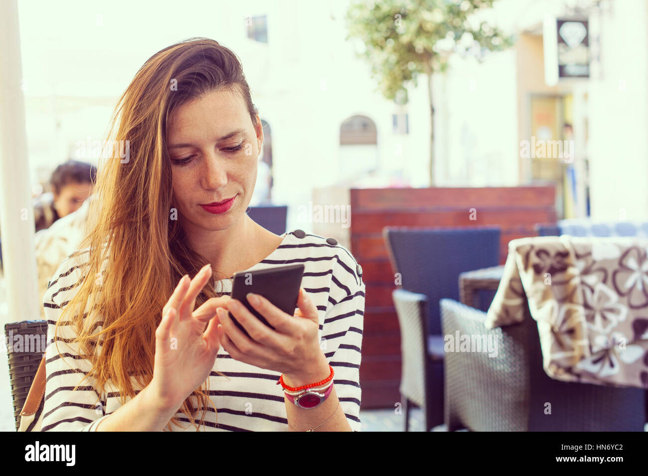 Young lady on bar table using a smart phone, dialing or using some app or sending sms, casual look, stripes shirt and light make up, hipster vintage c Stock Photo