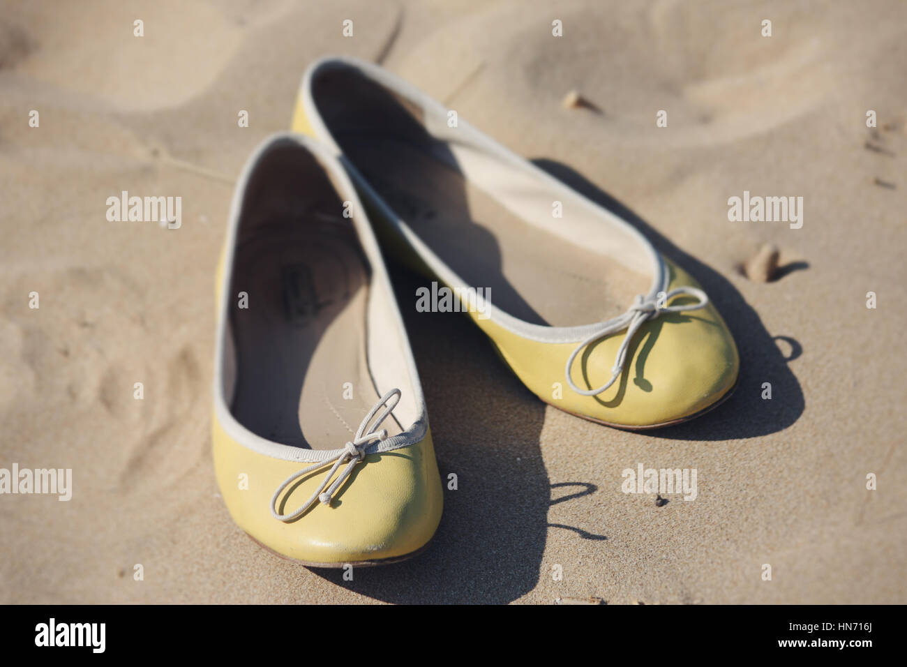 Yellow ballerina shoes lying on a sandy beach, while their owner bathed in the Mediterranean sea. Stock Photo