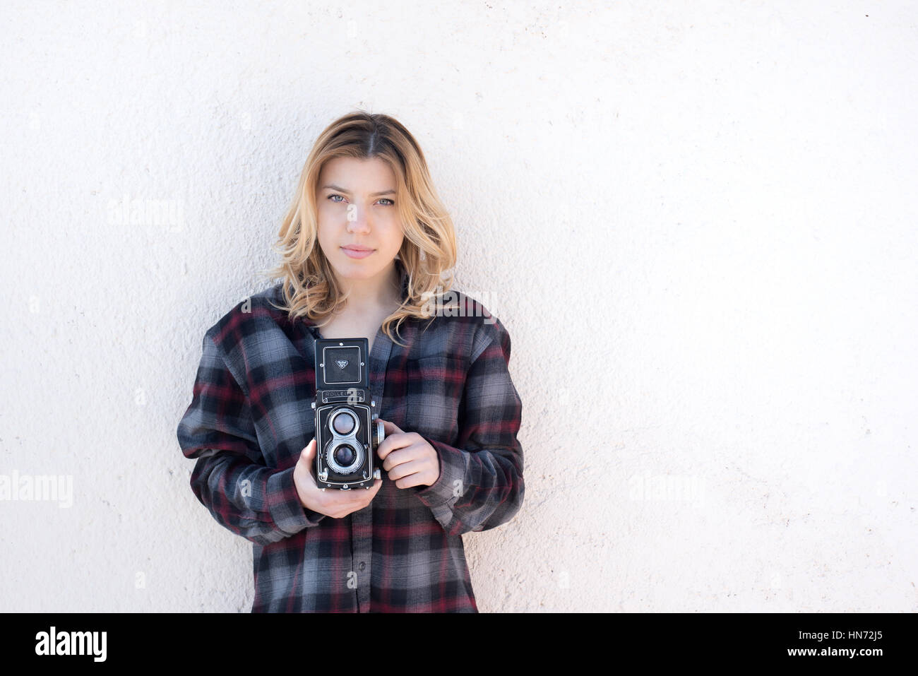 Young beautiful fascinating woman with old vintage Rolleflex camera portrait and neutral wall background Stock Photo