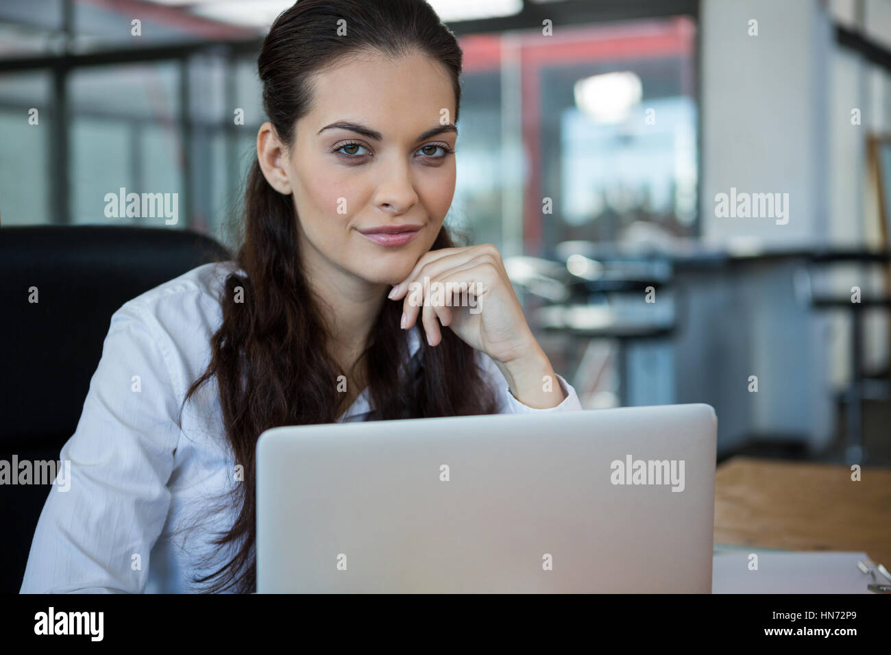 Portrait of female business executive sitting with laptop in office ...