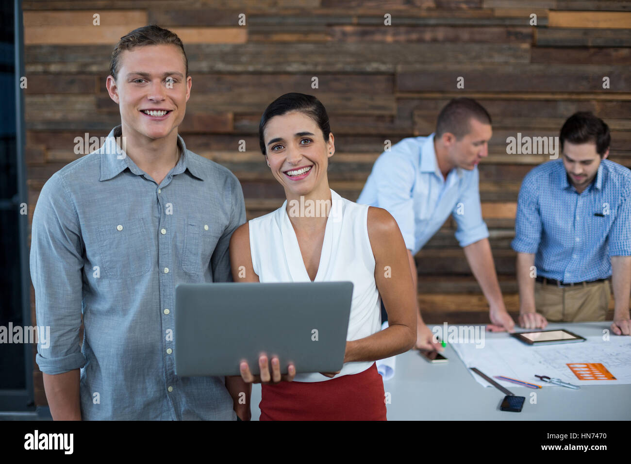Portrait of smiling business executives standing in office with laptop ...