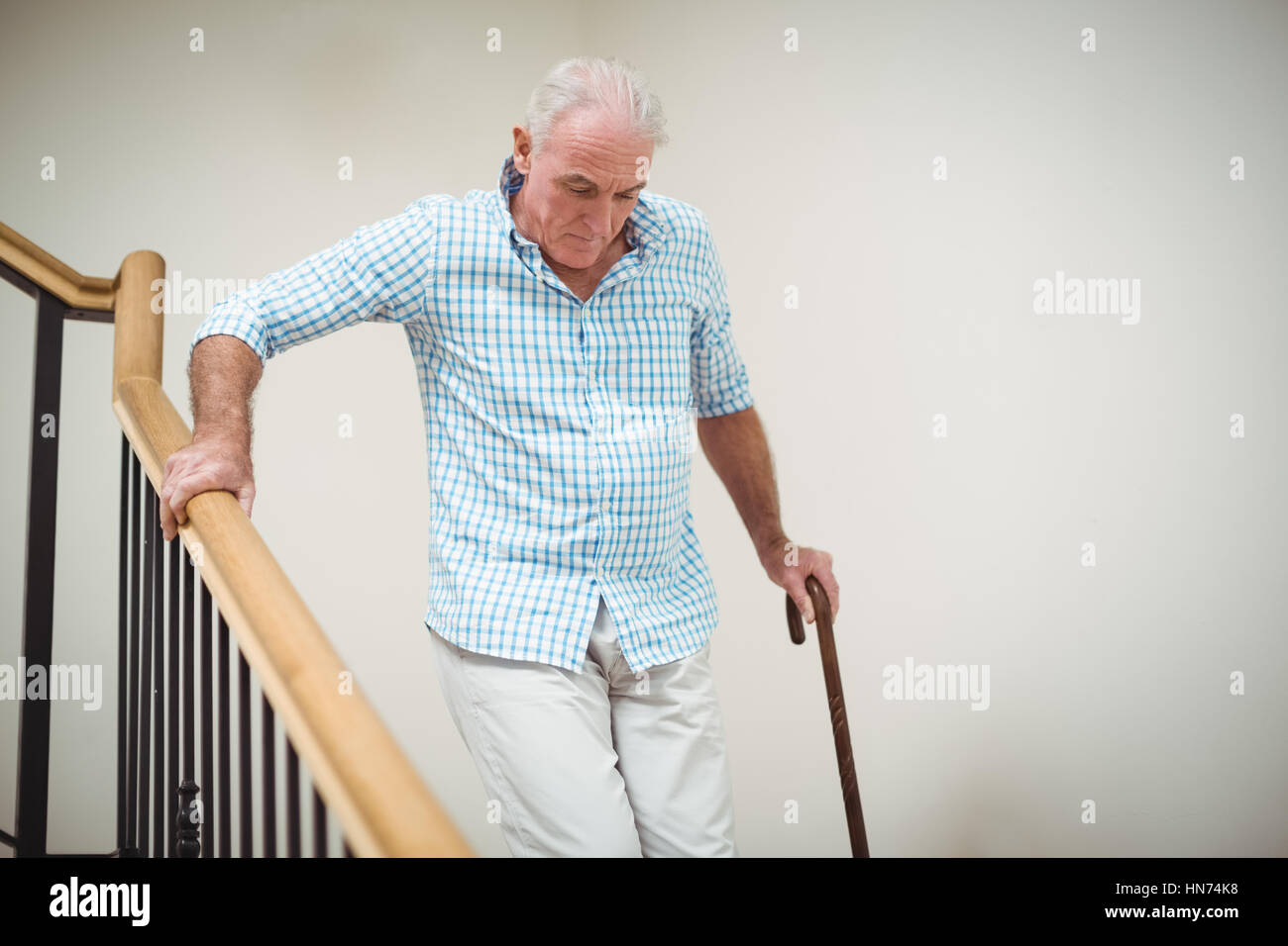 Senior man climbing downstairs with walking stick at home Stock Photo