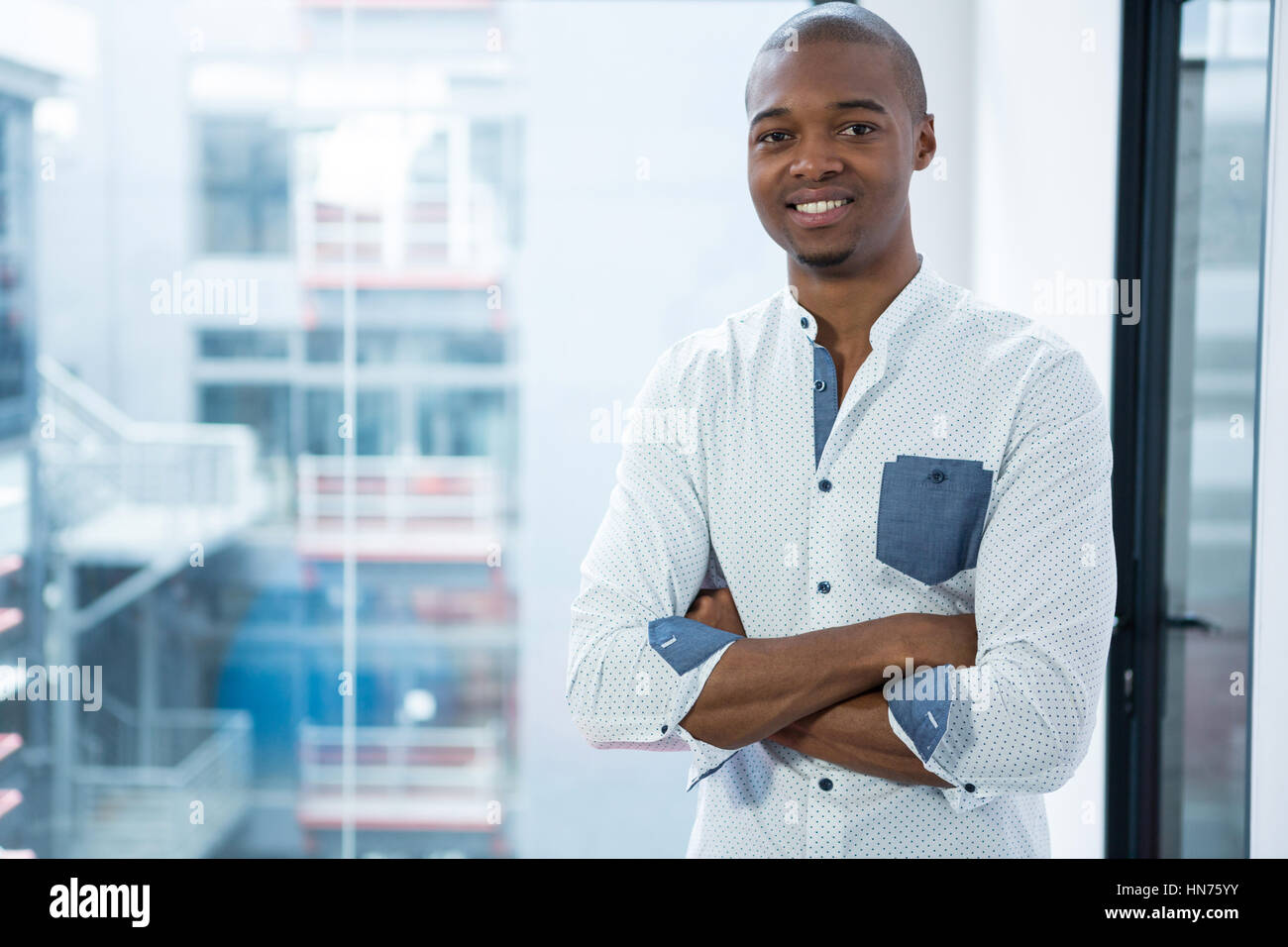 Portrait of smiling businessman standing with arms crossed in office ...