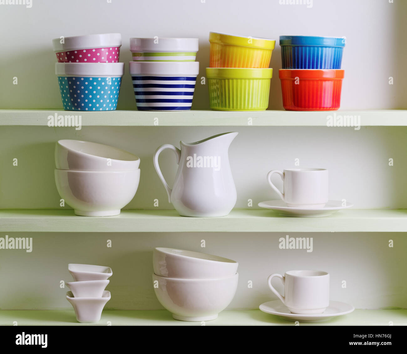 Variety of ceramics on shelf. Colorful bowls, cups and white dishware. Stock Photo