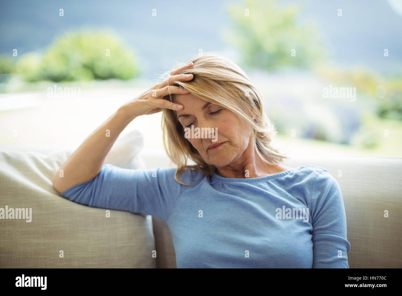 Tense senior woman sitting on sofa in living room at home Stock Photo