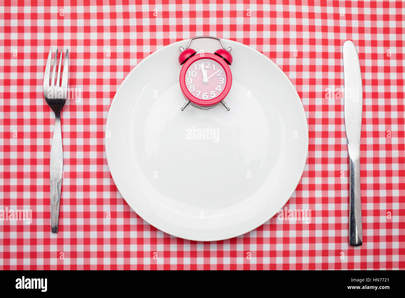 Time to lunch Concept : 12 o'clock Red Clock on white dish,knife and fork on red checker table cloth Stock Photo