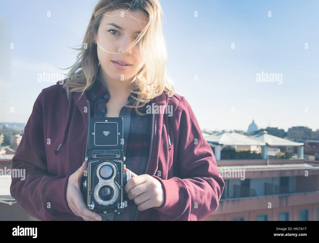 Rome, Italy - January 29 2017: Young beautiful fascinating woman with old vintage Rolleflex camera and Rome city skyline in background Stock Photo