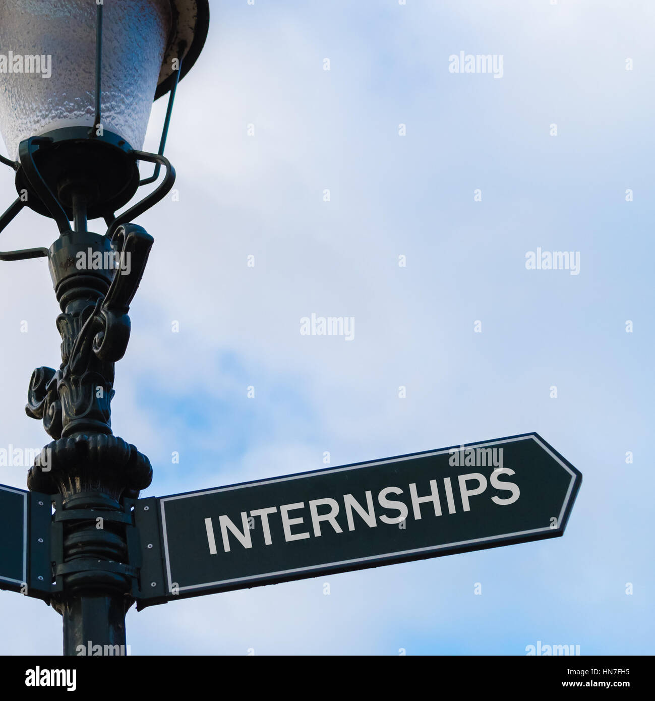 Street lighting pole with conceptual message INTERNSHIPS on directional arrow over blue cloudy background. Stock Photo