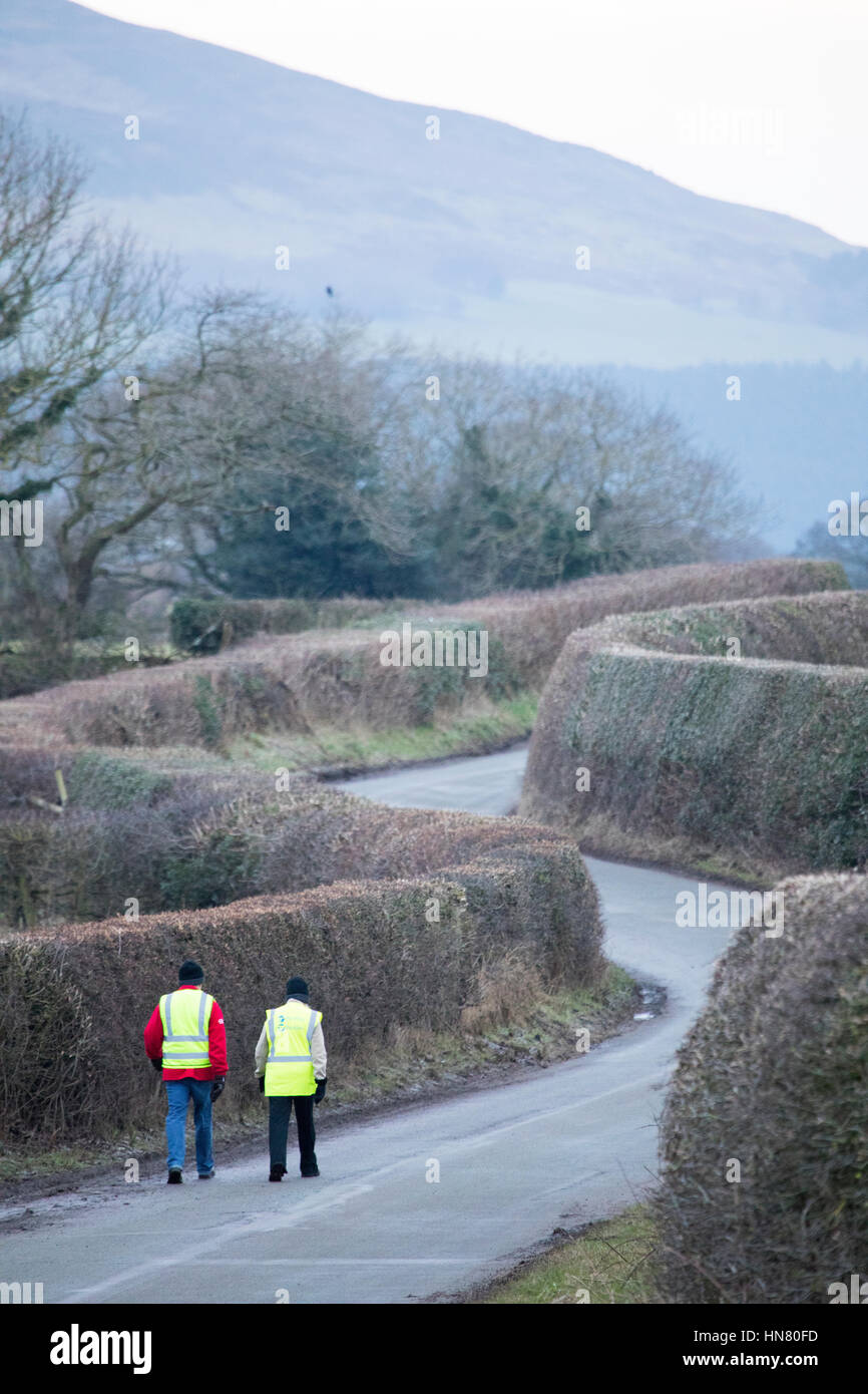 Two walkers in high visibility jackets walking down a narrow meandering