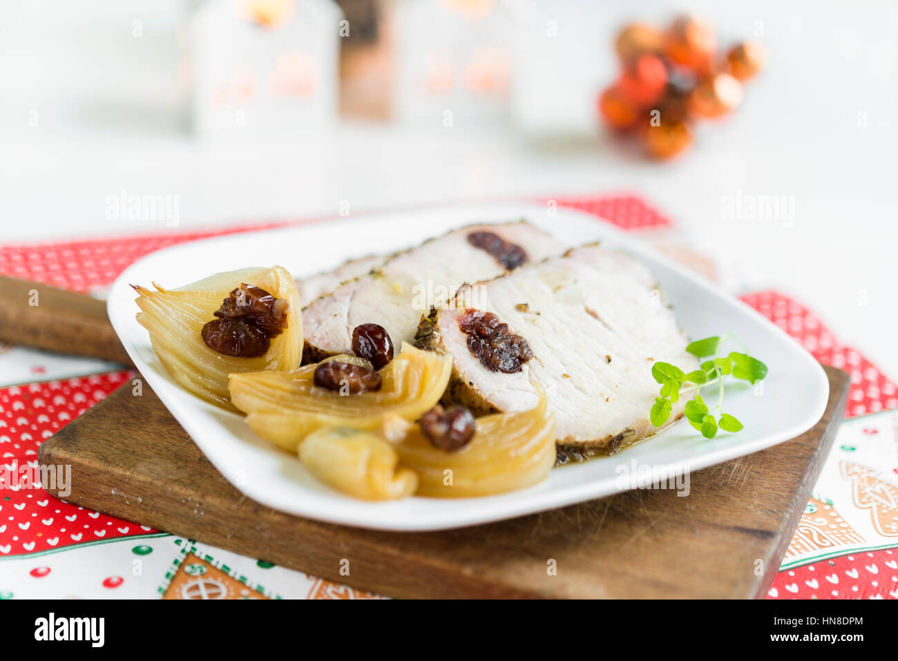 Slices of roasted pork chops stuffed with cranberries and garlic with cooked onion and fresh oregano on white plate arranged on rustic cutting board. Stock Photo