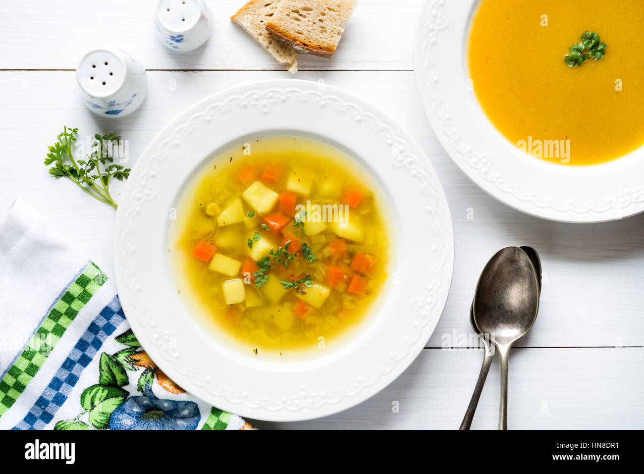 Two plates of vegetable soup and cream with bread fresh parsley, spoons, salt and pepper shakers on white wooden table Stock Photo