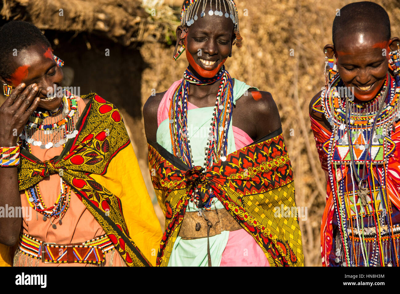 Three Maasai women, wearing traditional kangas, necklaces and earrings, laughing and smiling together in a village near the Masai Mara, Kenya, Africa Stock Photo