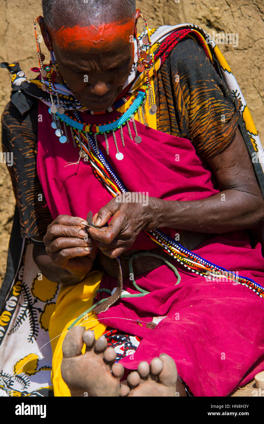 Maasai woman wearing traditional attire weaves beaded jewelry in a village near the Masai Mara, Kenya, East Africa Stock Photo