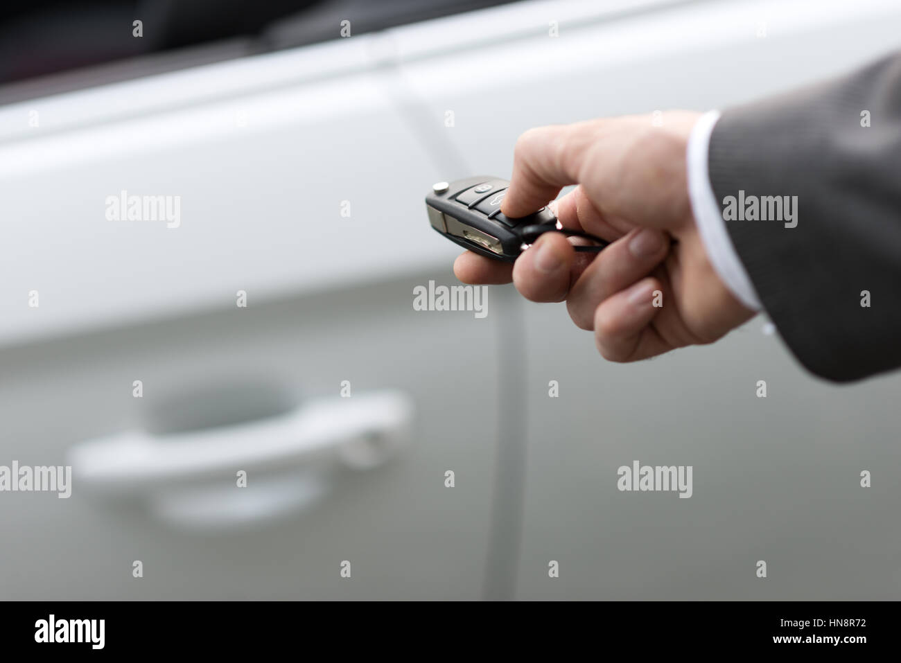 Businessman holding a car key with remote control and pushing a button, he is unlocking the door, hand close up Stock Photo