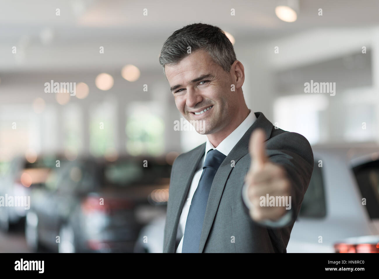 Car salesman at the showroom giving a thumbs up, dealership and sales concept Stock Photo