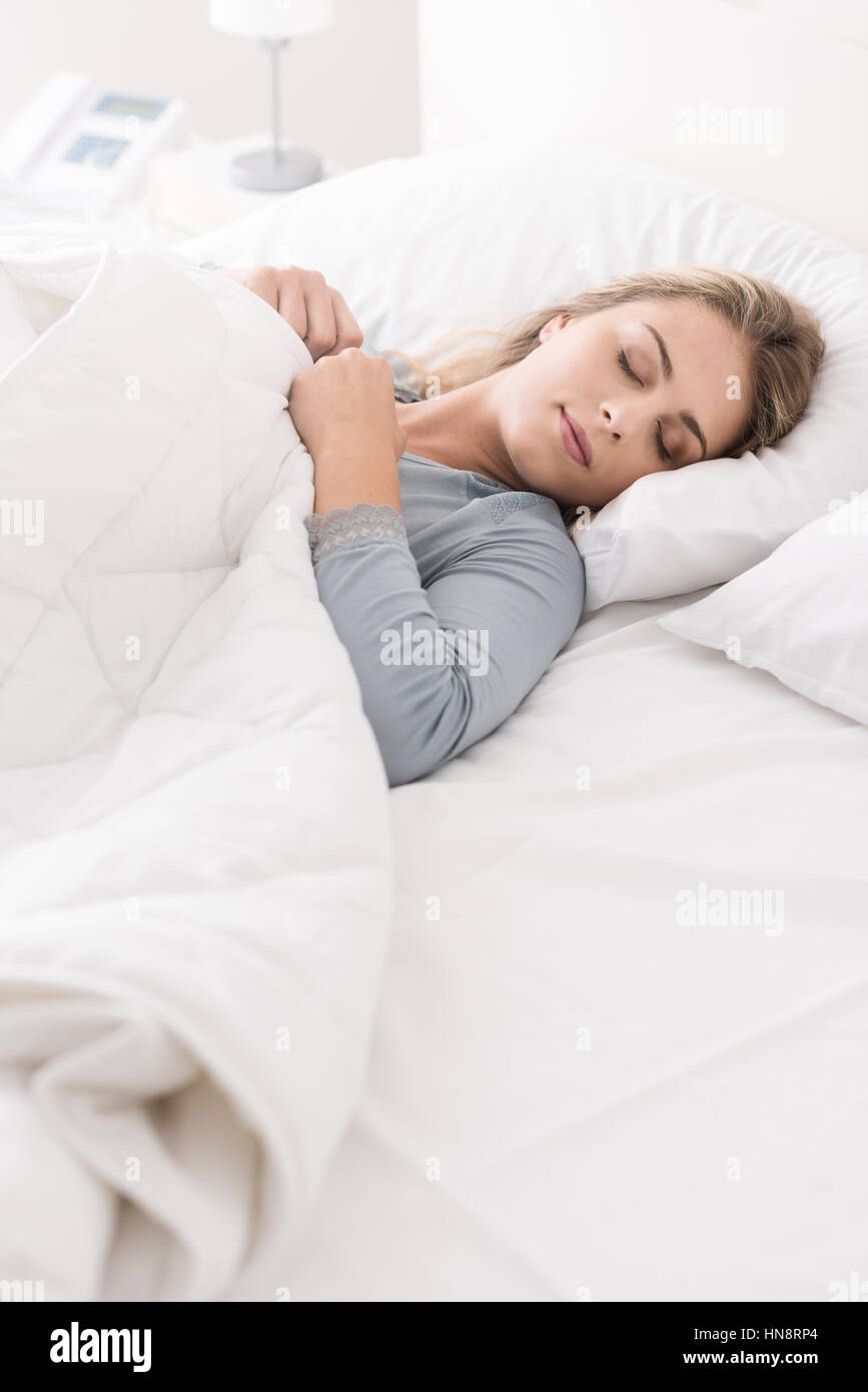 Young beautiful woman sleeping in the bed, she is relaxing and dreaming with eyes closed, she is covering herself with a soft duvet Stock Photo