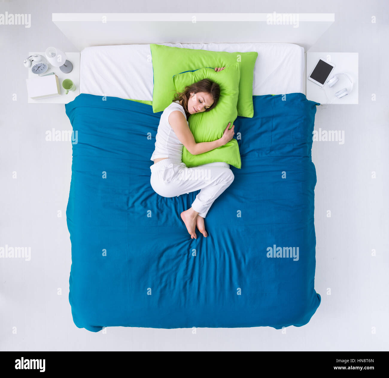 Young woman sleeping in her bedroom, she is curling up on the duvet and hugging a pillow Stock Photo