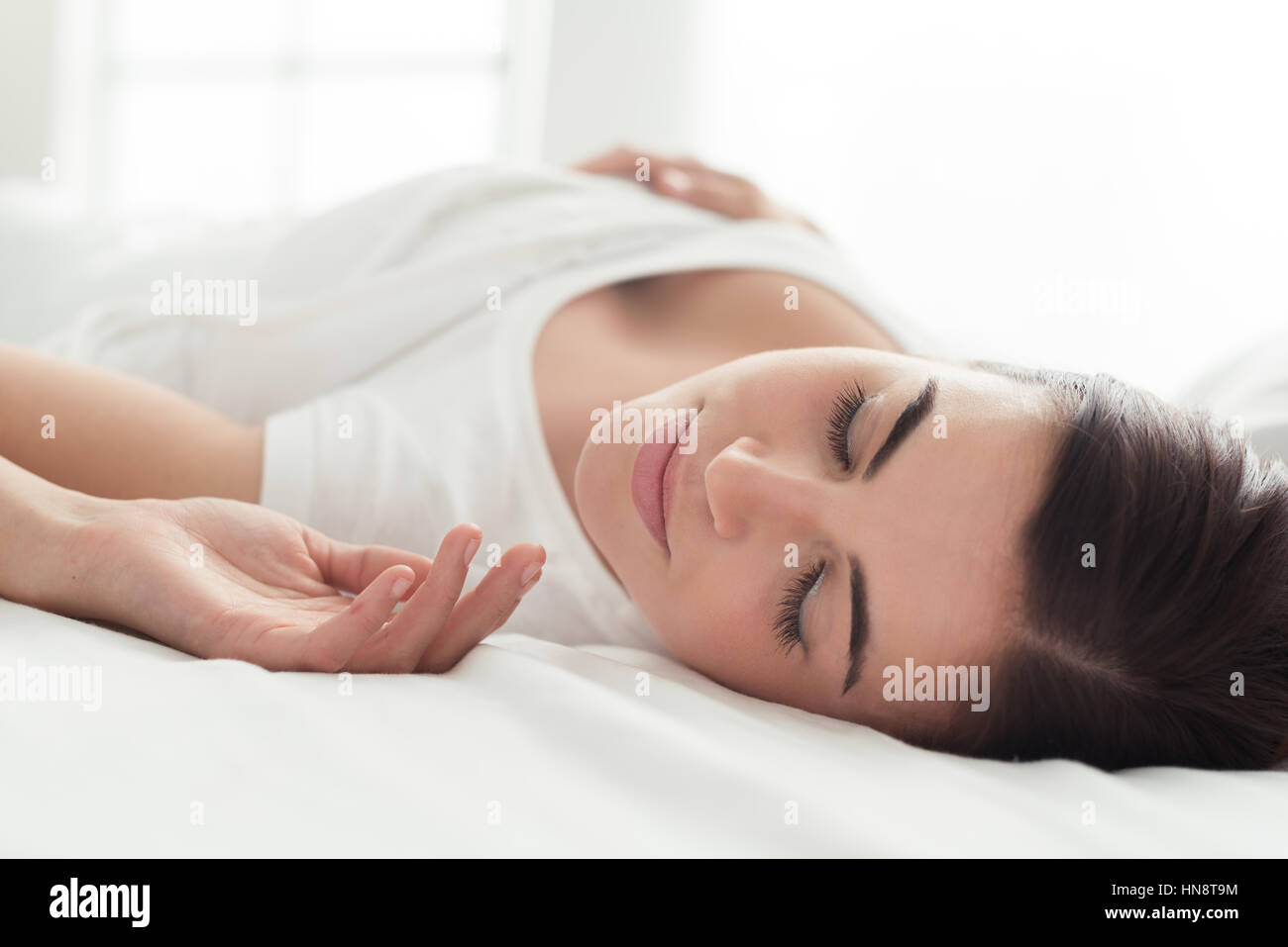 Beautiful smiling woman lying down in bed and relaxing, she is sleeping with eyes closed Stock Photo