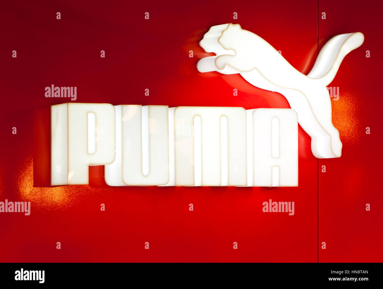 Dusseldorf, Germany: White illuminated PUMA logo on red wall at sportswear shop at DUS airport. Stock Photo