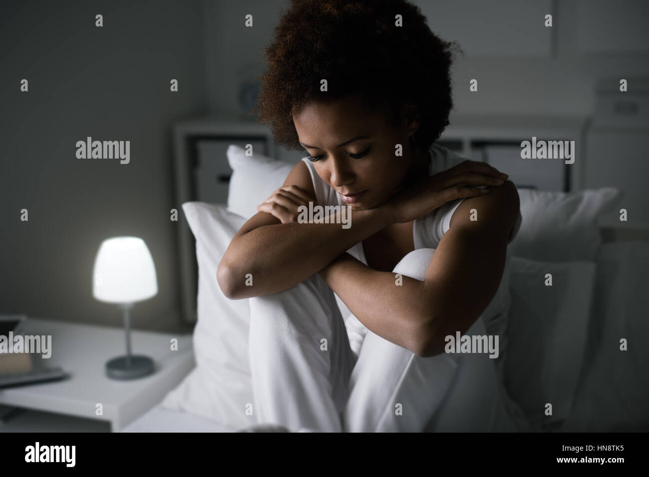 Sad depressed woman sitting in her bed late at night, she is pensive and suffering from insomnia Stock Photo