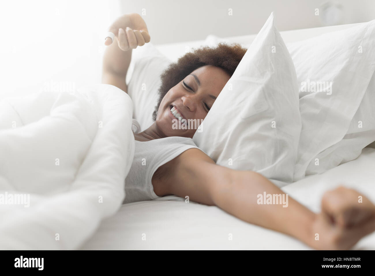 Beautiful woman waking up in her bed, she is smiling and stretching Stock Photo