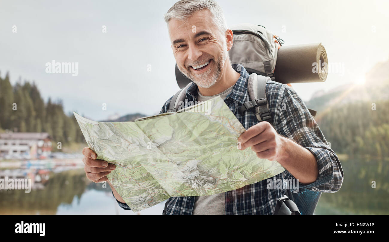 Smiling mature hiker trekking on the mountains and searching directions on a map, sports and travel concept Stock Photo