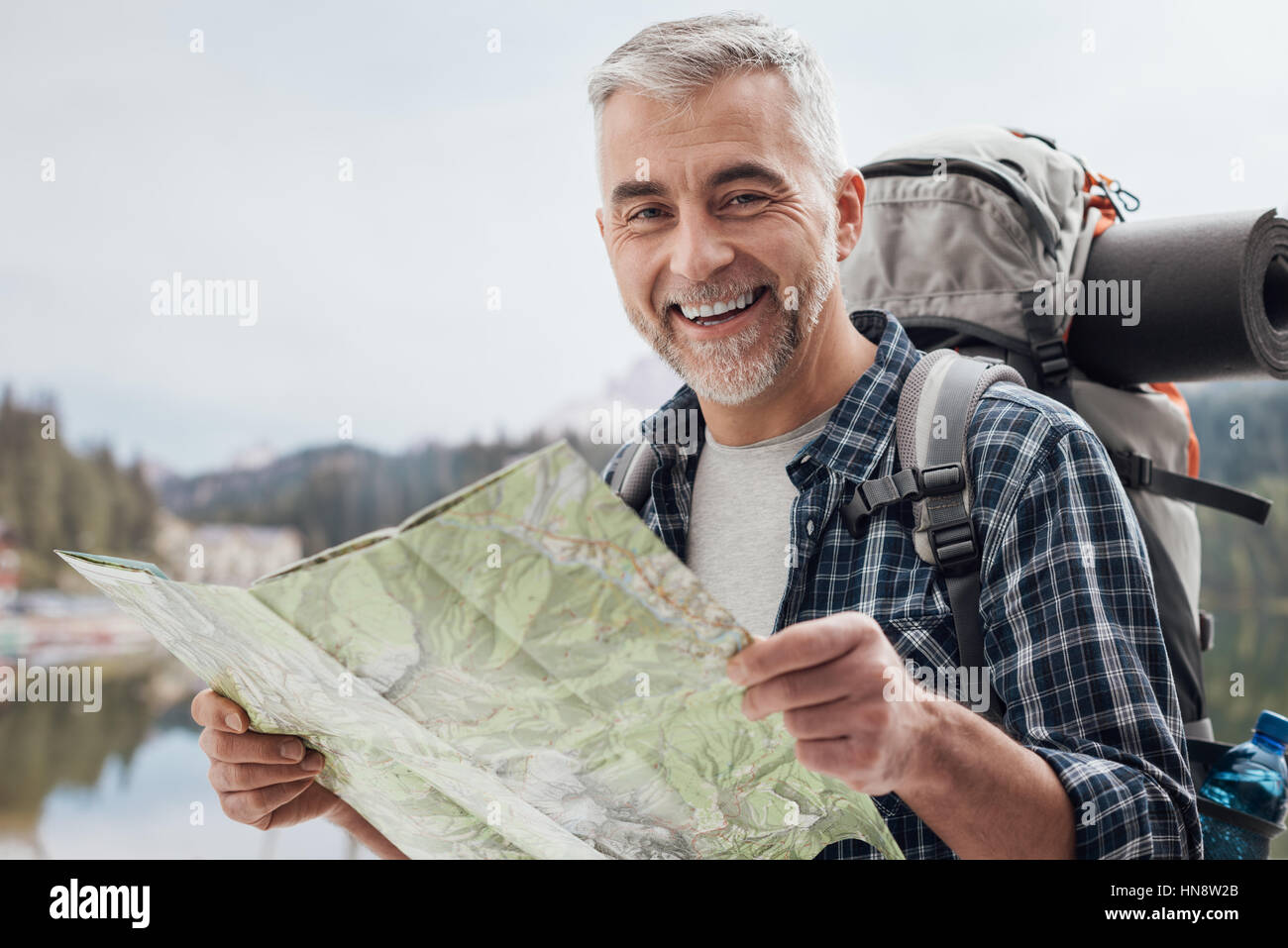 Smiling mature hiker trekking on the mountains and searching directions on a map, sports and travel concept Stock Photo