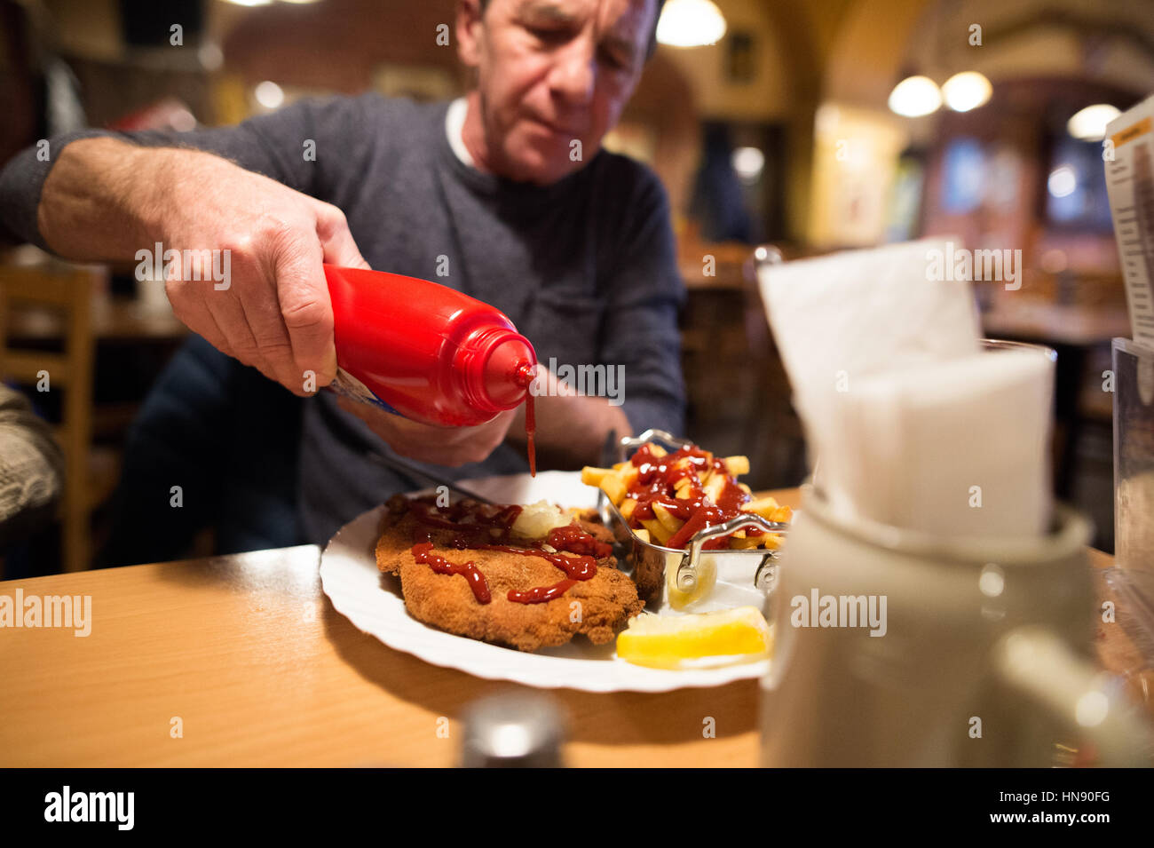 Senior man in restaurant puts ketchup on fries and schnitzel Stock Photo