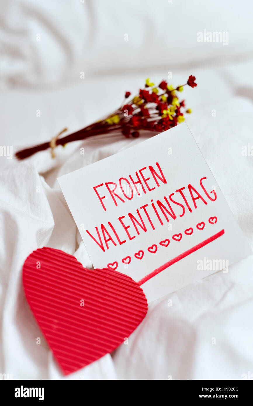 closeup of a red heart, a white paper note with the text frohen valentinstag, happy valentines day written in german, and a bunch of dry flowers on th Stock Photo