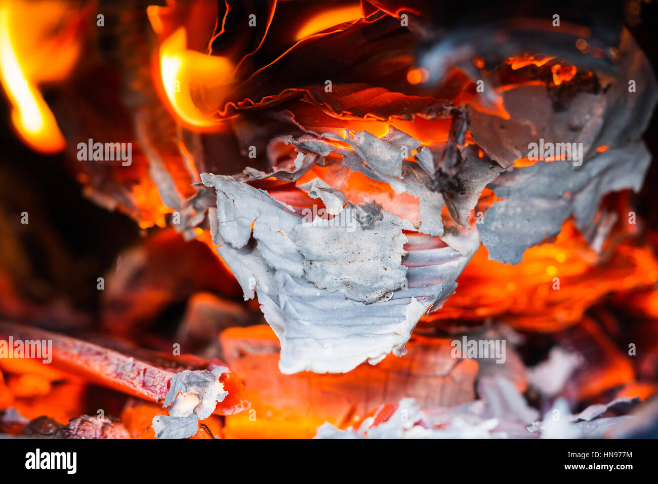 Sheets of paper burn and smolder in a stove among wooden planks and