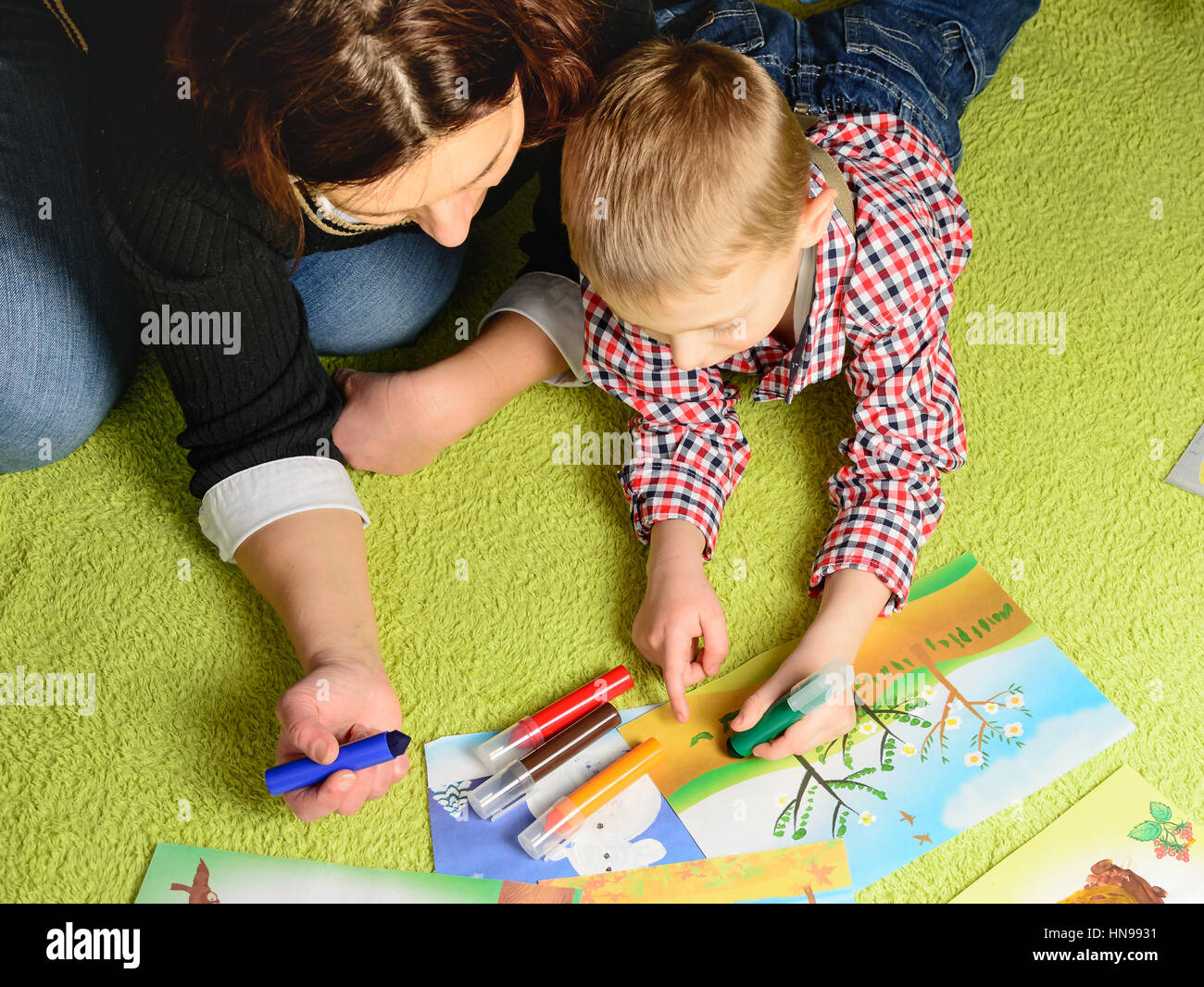 the child together with mother draws a picture lying on a green carpet Stock Photo