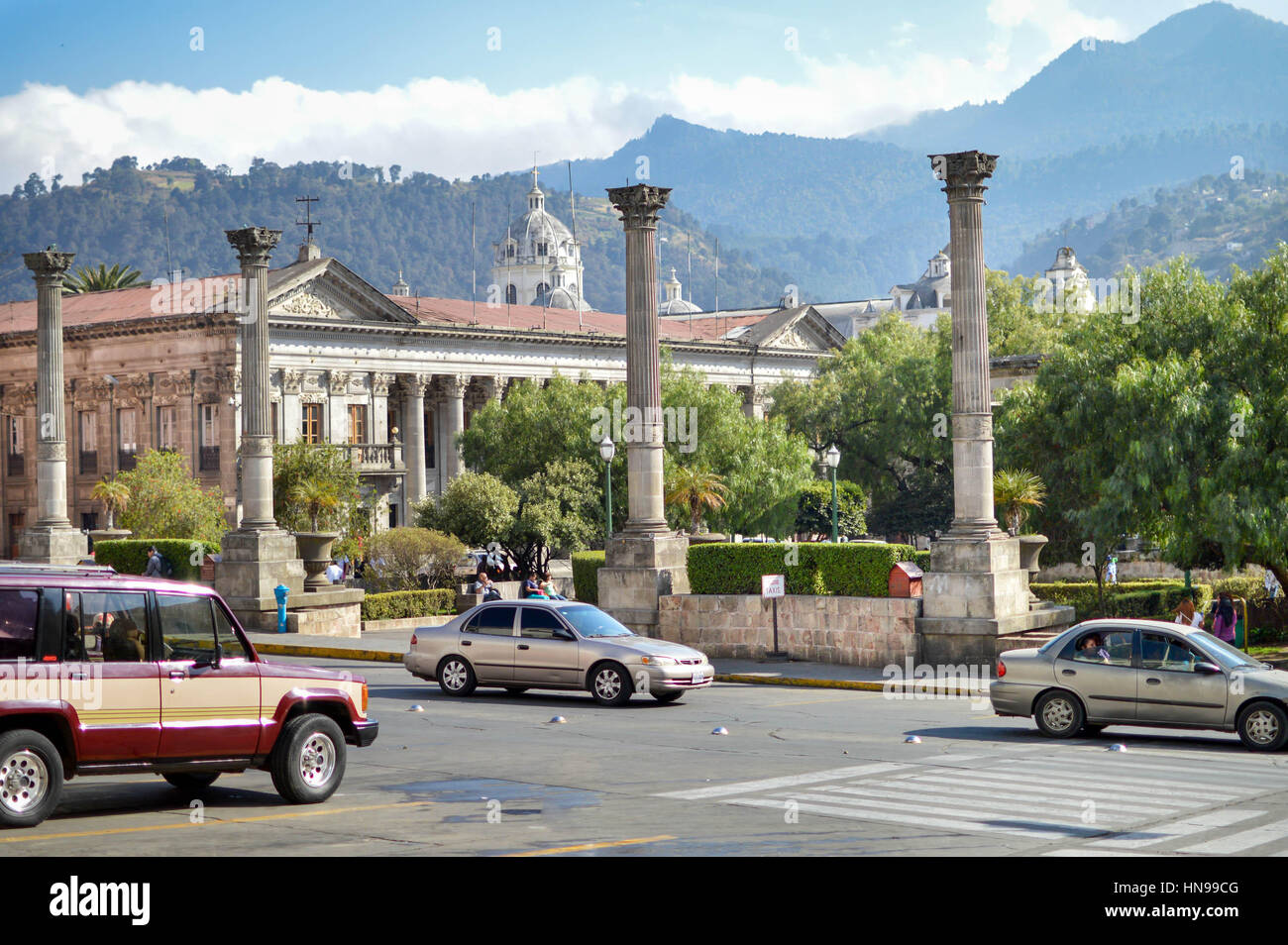 Cars pass by the central plaza of the historic center of Quetzaltenango, aka Xela, in Guatemala. Municipal palace and mountains  on the background Stock Photo