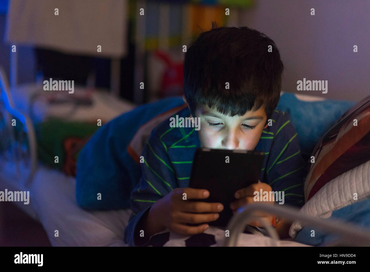 Boy plays on computer tablet in bed Stock Photo