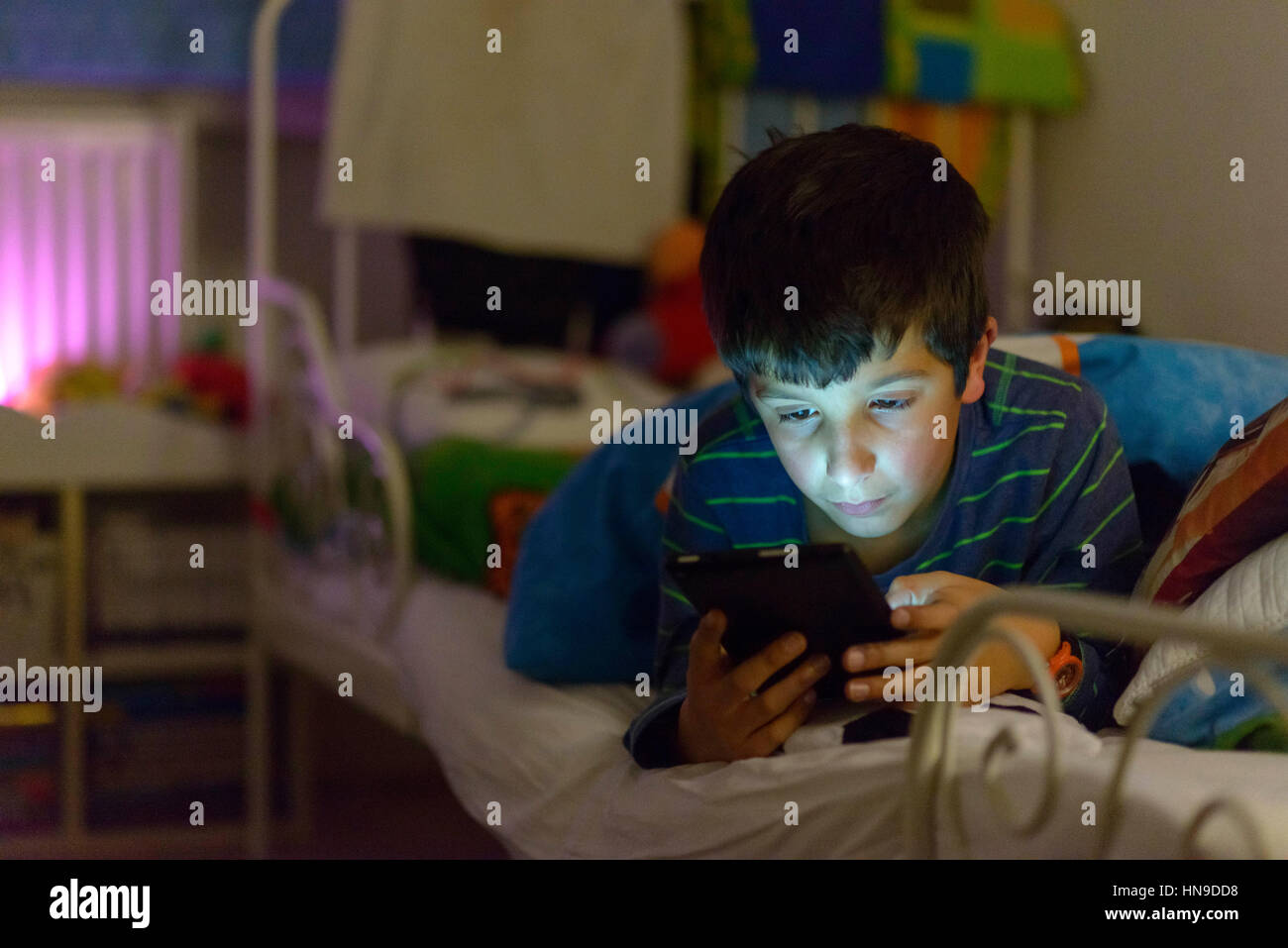 Boy plays on computer tablet in bed Stock Photo