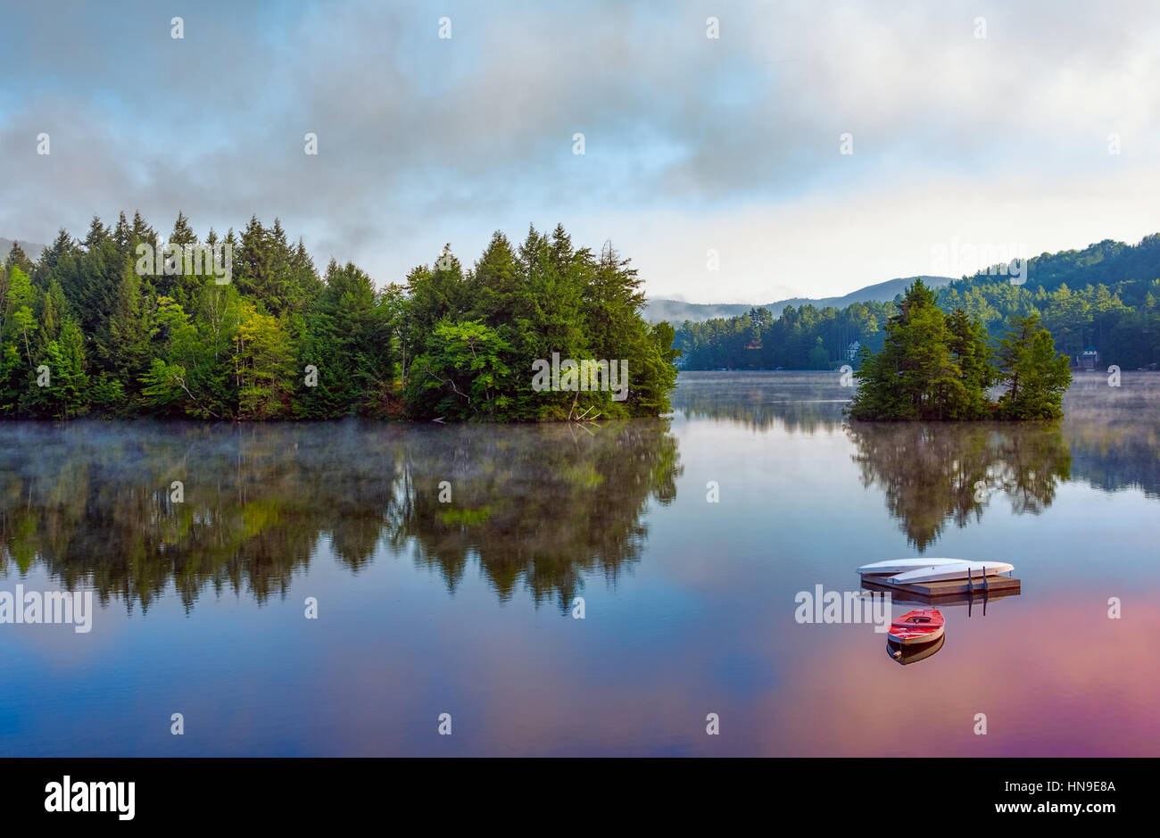 A lake in the early morning with fog on the water. A boat and dock are ...
