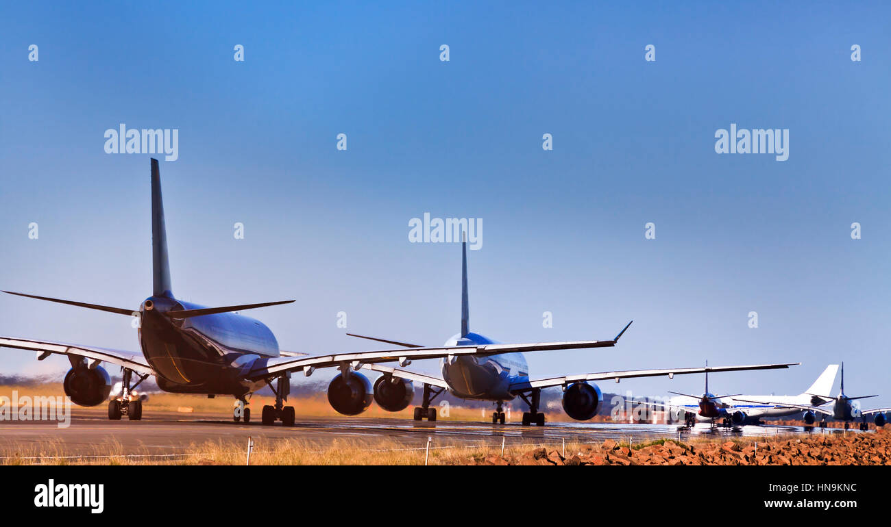 5 commercial airplanes lining up on runway of airport airfield waiting for departure. Clear sky above Sydney International airport and land jet traffi Stock Photo