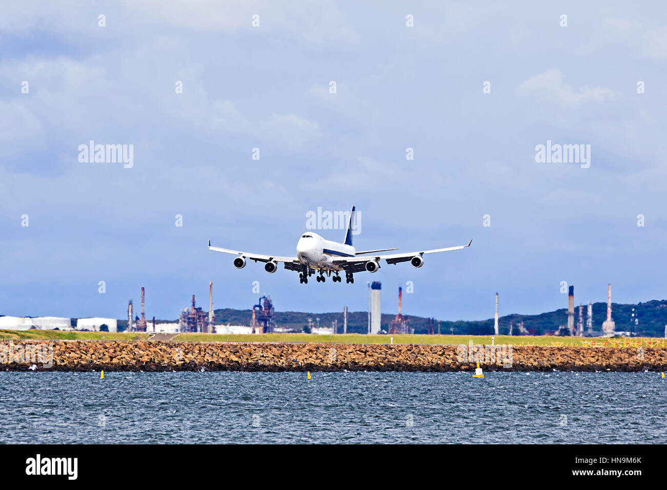 Huge jet airplane landing on Airport runway in Sydney against cargo terminal and blue sky. Stock Photo
