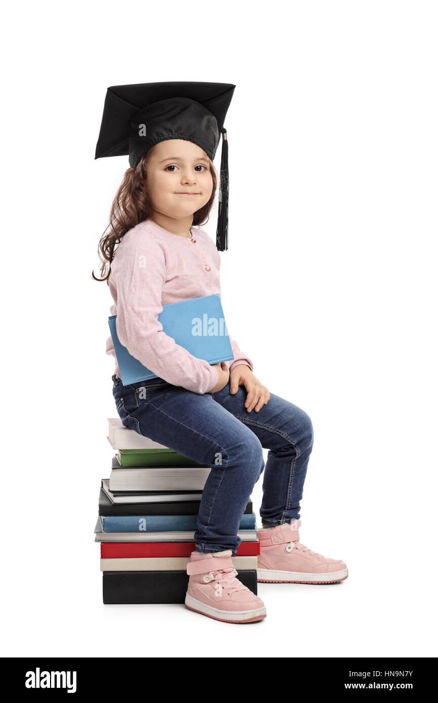 Little girl with a graduation hat sitting on a pile of books isolated on white background Stock Photo