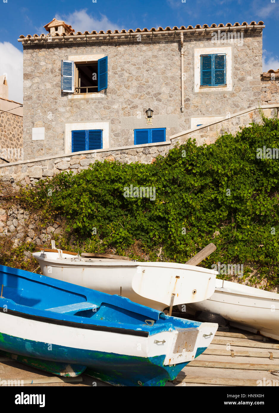 Waterfront house in small fishing village in Majorca Spain with blue shutters and a blue boat in foreground. Stock Photo