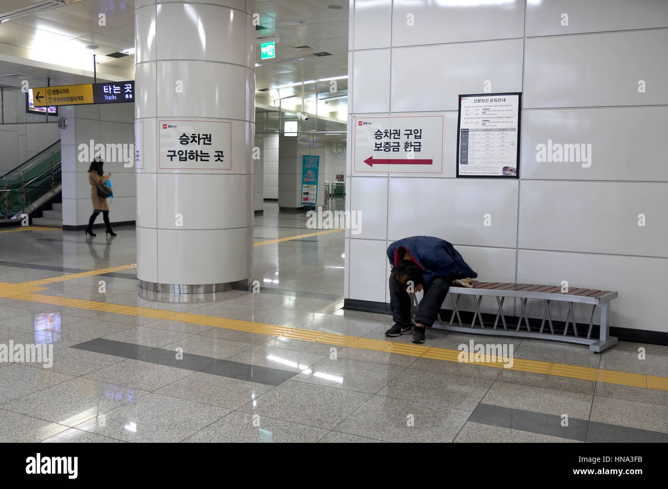 Woman texting on smartphone and homeless man sleeping on a bench in underground subway train station. Seoul, South Korea, Asia Stock Photo