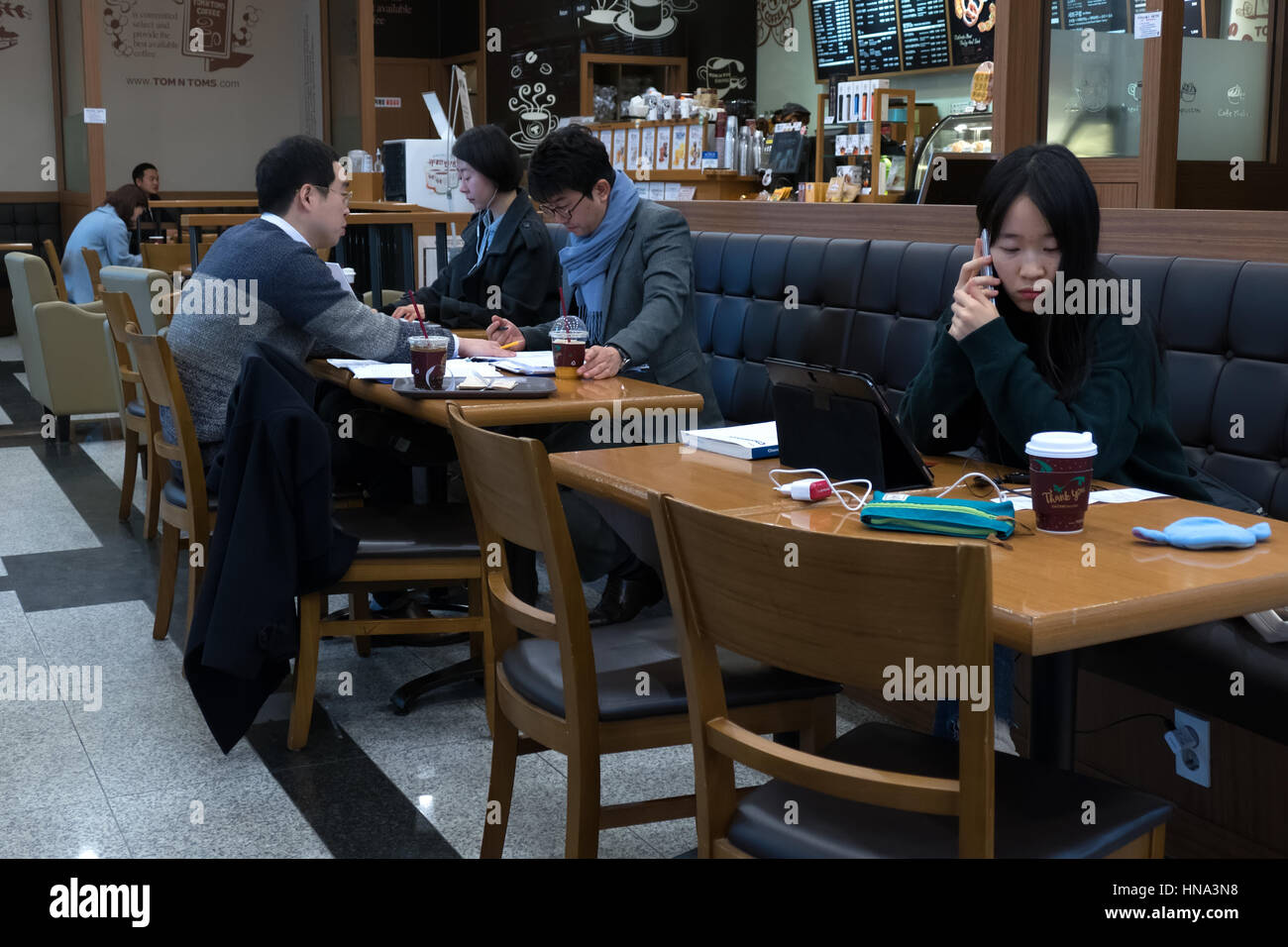 Young Korean student studying with phone and ipad tablet, Asian people working in a cafeteria, busy businessmen with papers. Seoul, South Korea, Asia Stock Photo