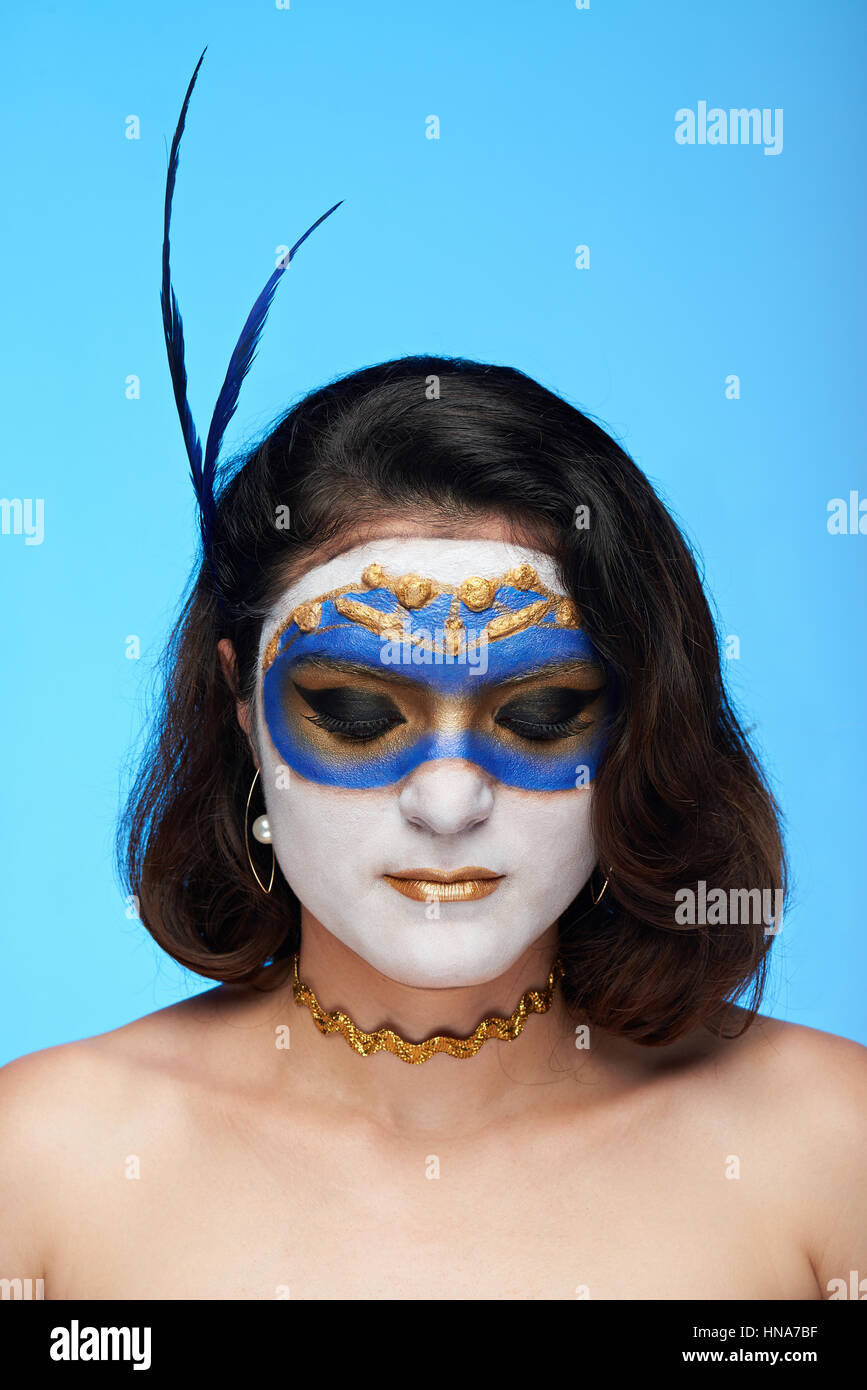 bodyart on women white face of golden mask isolated on blue background Stock Photo